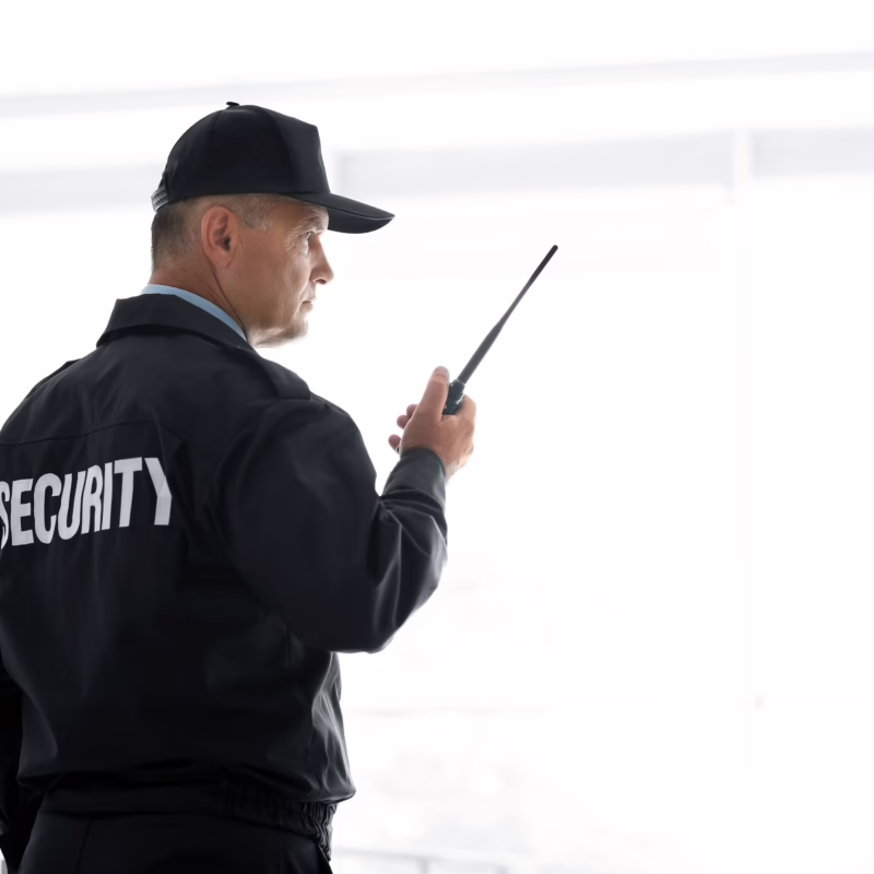 private security officers standing at the entrance of a modern commercial building. Both officers face outward in a professional stance, each holding a ruggedized black two-way handheld radio at chest level.